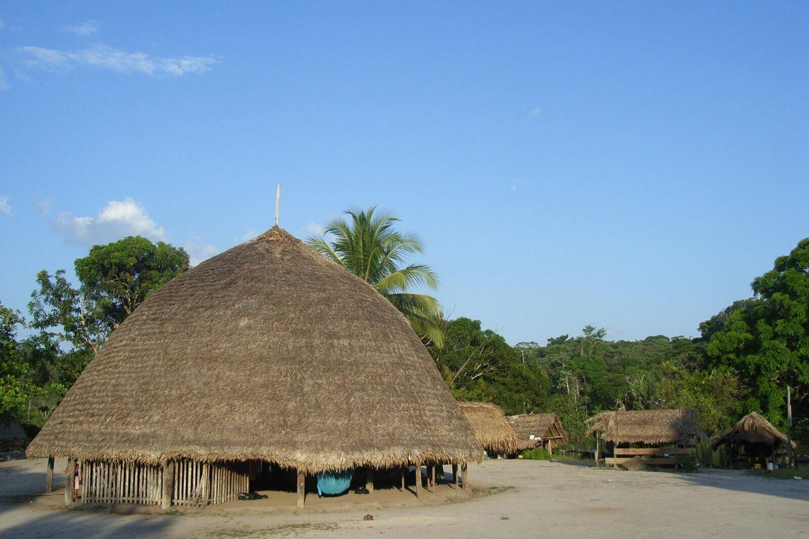 Grote ronde dorpshal met rieten dak op een open zandplein in een dorp aan de rivier.
