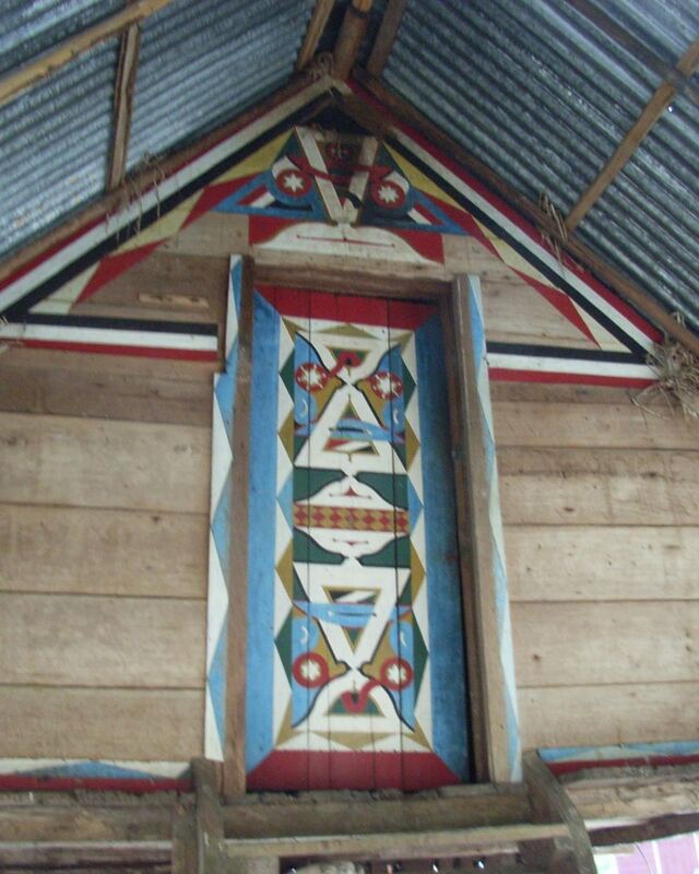 Beschilderde houten topgevel met geometrische tembe-motieven in blauw, rood en wit.